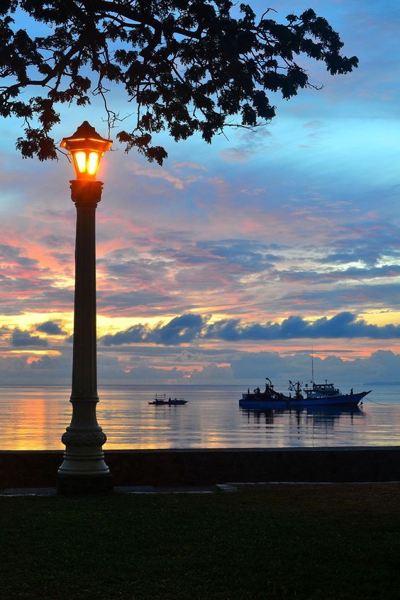 a lamp post in front of the ocean at sunset