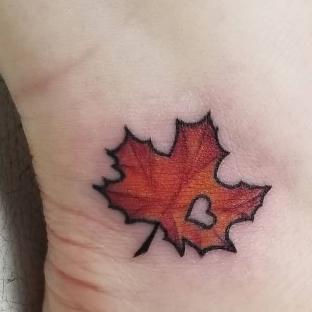 a small leaf tattoo on the side of a woman's leg, with two hearts in it