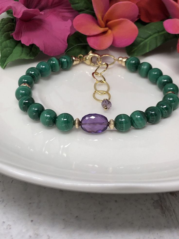 This unique beauty features AAA, gorgeously swirl malachite. Ripples of soft emerald and forest green add such amazing details to these gemstones. And what better to complement the verdant hues than a deep, violet amethyst with sparkling facets! Everything is intricately handcrafted in 14k yellow gold filled. An oval extender chain and plump amethyst drop finish this exquisite bracelet. Bracelet is adjustable from approximately 6.75 to 7.75 inches. - These are natural gemstones, please allow for Elegant Malachite Round Beads Bracelets, Gold Malachite Jewelry Hand-strung, Hand-strung Gold Malachite Jewelry, Elegant Hand-strung May Birthstone Beaded Bracelets, Elegant May Birthstone Beaded Bracelets, Elegant Malachite Beaded Bracelets For Gift, Elegant Handmade Malachite Bracelets, Malachite Gemstone Bracelet, Elegant Hand-strung May Birthstone Bracelets