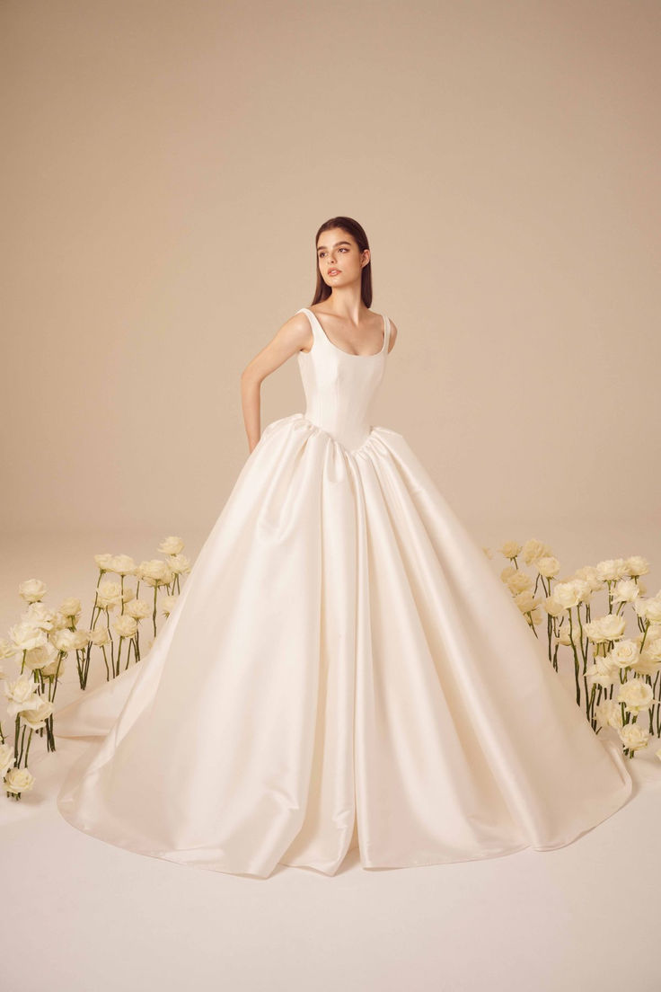 a woman in a white wedding dress standing next to flowers and looking at the camera