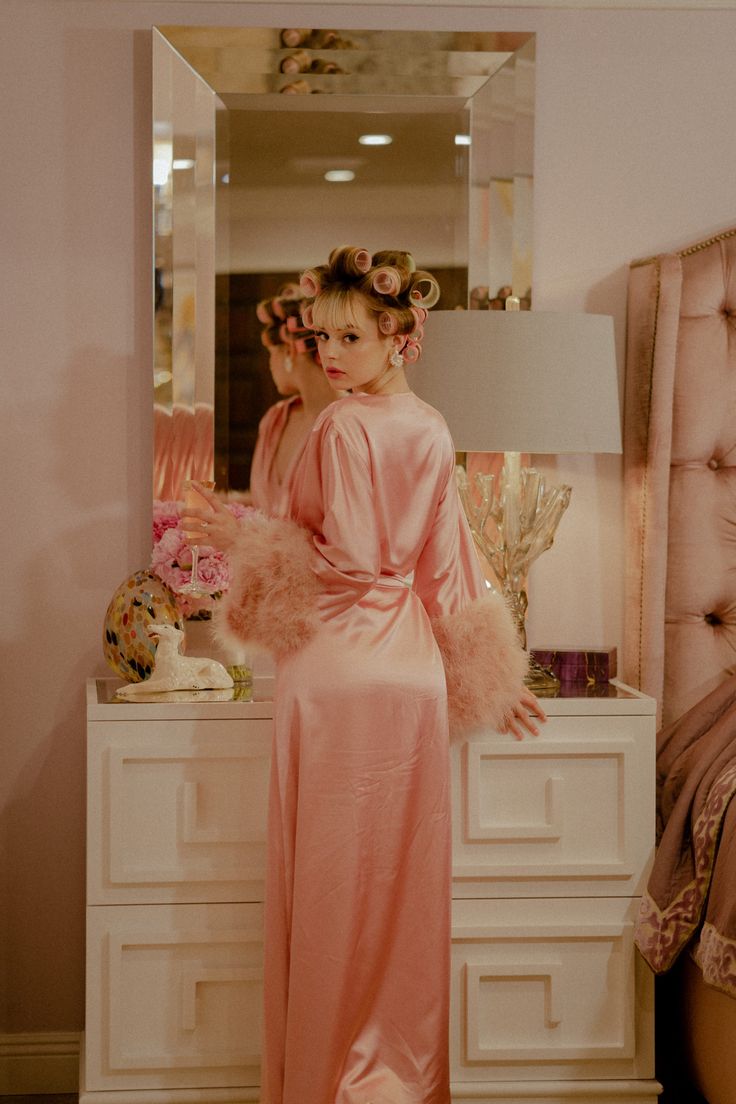 a woman standing in front of a mirror wearing a pink dress with feathers on it