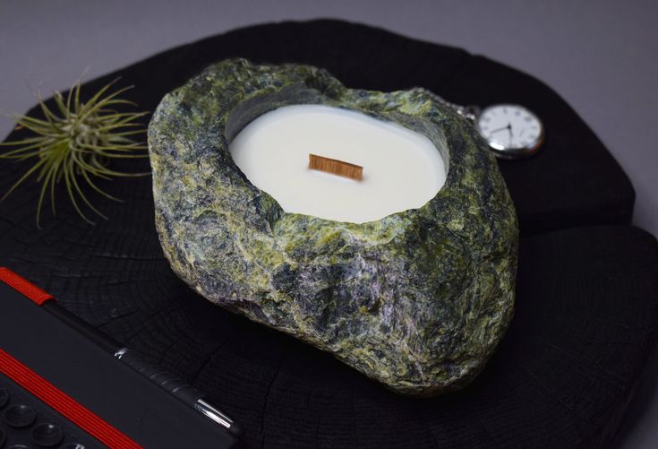 a rock with a lit candle on it next to a small air plant and a pocket watch