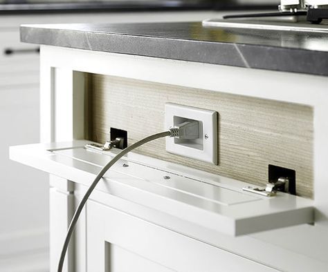 an electrical outlet plugged into the wall in a kitchen with white cabinets and drawers