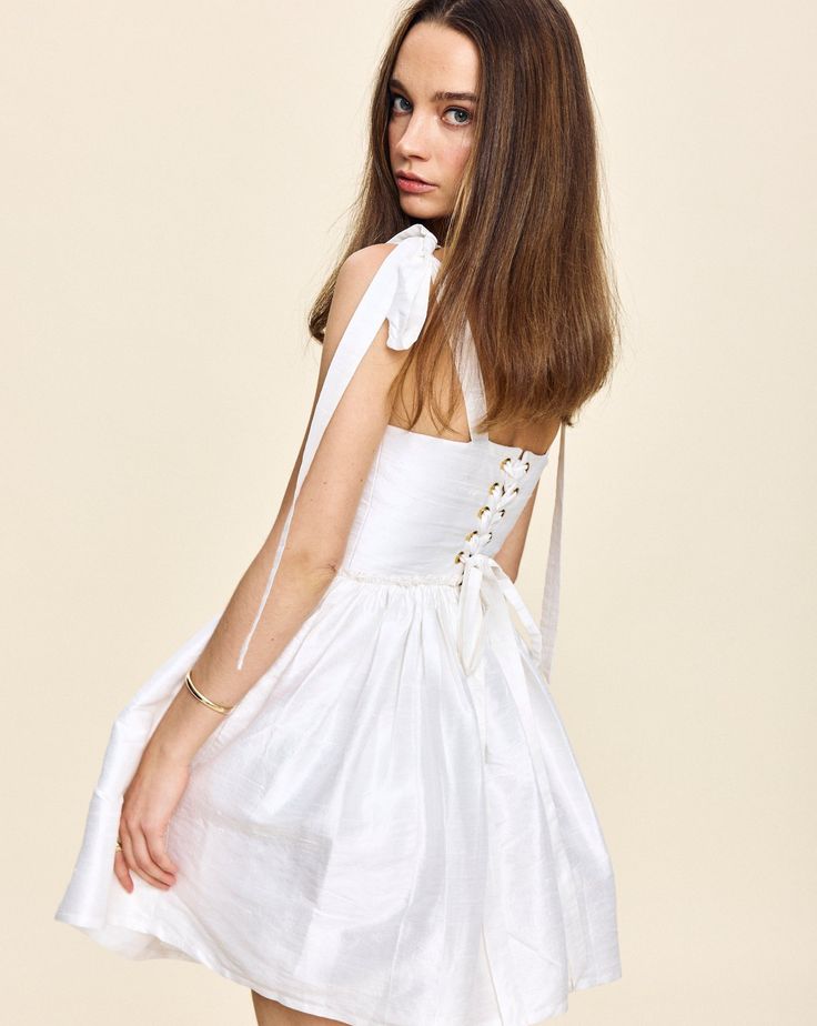 Louise New York creates its collection with the past and present in mind. Inspired by timeless glamour instead of trends, when you slip into a Louise New York dress, you carry all the confidence and carefree attitude that femininity can acclaim. Get best dressed with the Marie Mini Dress in White. This silhouette features a signature corset lace-up back to fit any waist, and boasts a bust with ties at the shoulder for an even more custom fit. Product Details Taffeta. Made in NYC. Care Instructio Elegant A-line Mini Dress With Tie Straps, Evening Mini Dress With Tie Straps, Knee-length Dresses With Tie Straps For Day Out, Feminine Summer Mini Dress With Corset Back, Feminine Summer Dresses With Corset Back, Elegant A-line Mini Dress With Lace-up Back, Feminine Cocktail Mini Dress With Tie Back, Sleeveless Dress With Lace-up Back For Day Out, Flirty Dress With Lace-up Back For Brunch