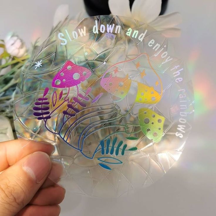 a hand holding a clear glass ornament with colorful designs on it and saying slow down and enjoy the world