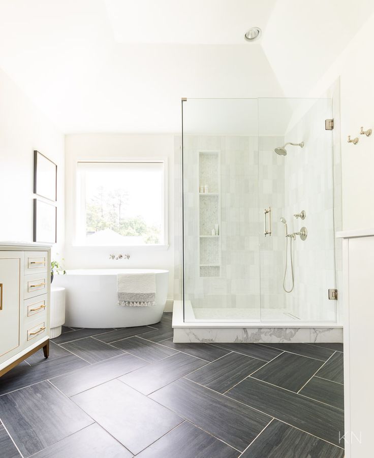 a white bathroom with black tile flooring and a bathtub next to a window