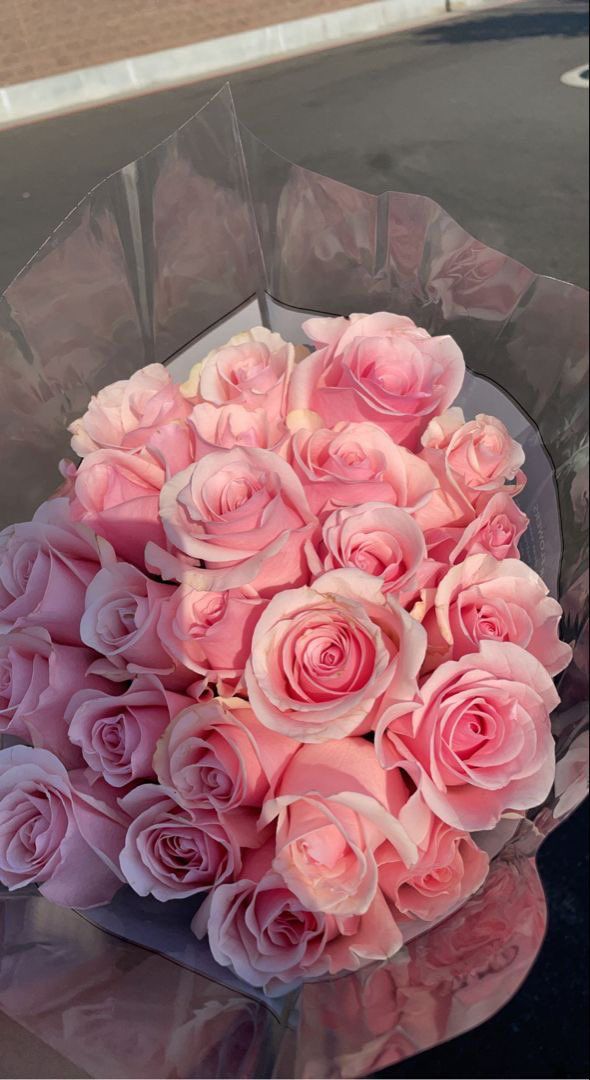 a bouquet of pink roses sitting on top of a car hood in front of a building