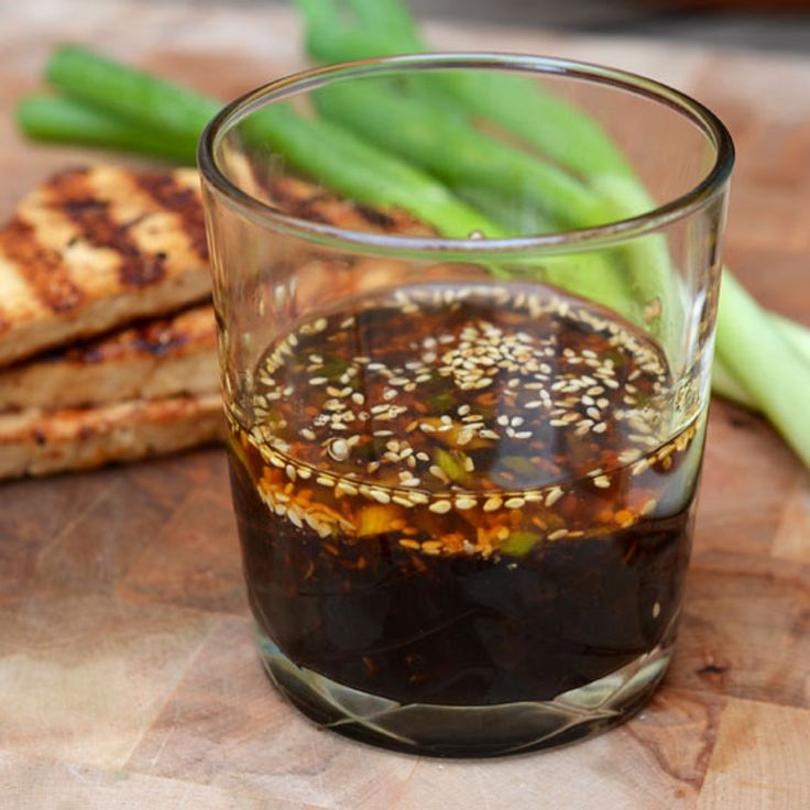 a glass filled with sauce next to some green beans and meat on a cutting board