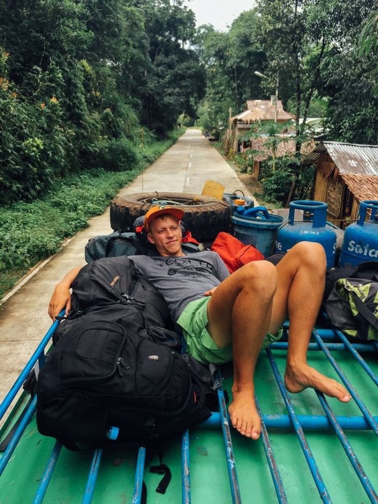 a man laying on the back of a truck with lots of luggage strapped to it