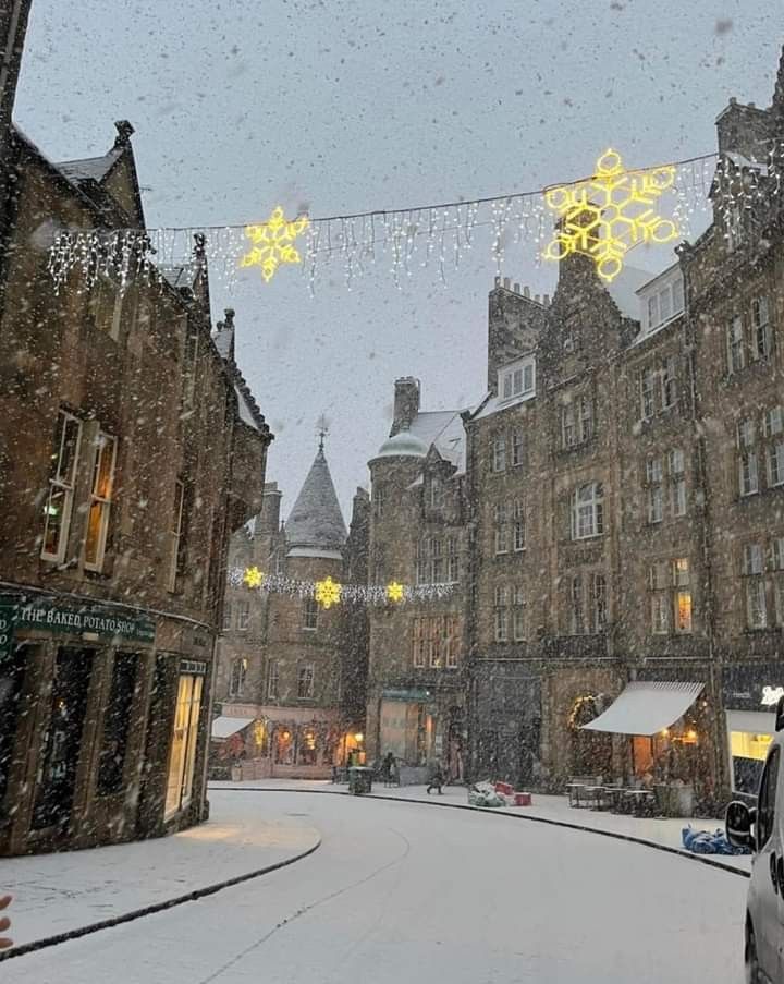 a city street is covered in snow with christmas lights strung from the buildings and decorations