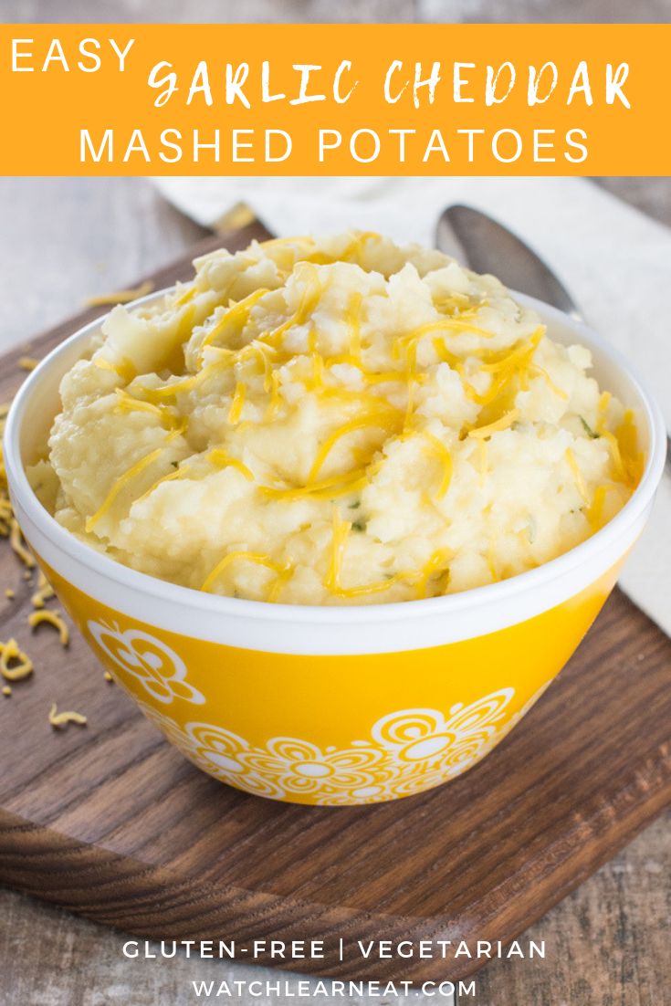 a yellow bowl filled with mashed potatoes on top of a wooden cutting board