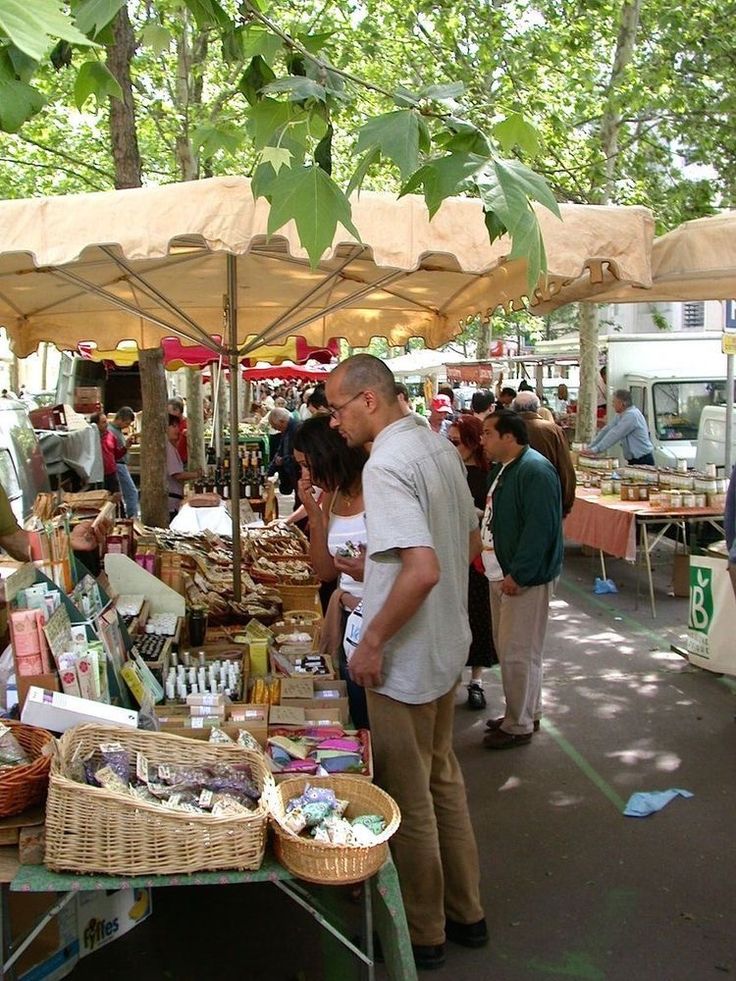 people shopping at an outdoor market with umbrellas and tables full of goods for sale