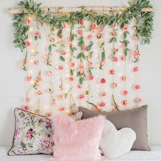 a white bed topped with pillows next to a wall covered in flowers and greenery