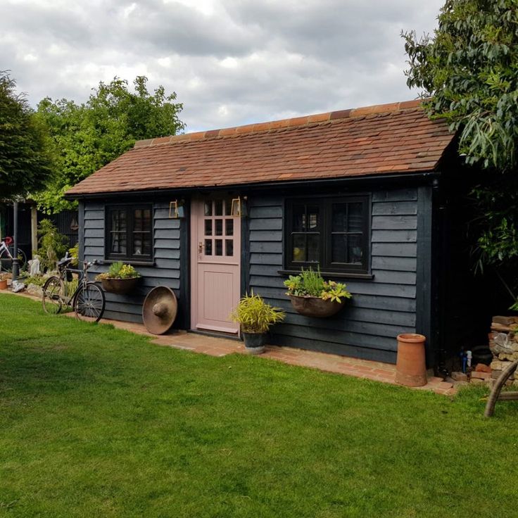 a small gray shed with potted plants on the side and a bicycle parked in front