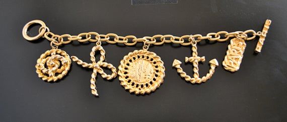 ***The bracelet is made with 5 large plated gold charms. ***Necklace has the same charms plus 4 faux pearls. ***Charms include a ribbon, anchor, "PARIS," and two medallions. ***One of the medallions has a Fleur De Lis design on it. ***Great runway bracelet and necklace. Attention grabber. ***Bracelet is Secure the bracelet by passing the last bar charm through the ring. ***Bracelet is 7'' long (untied.) ***The largest charm is 1.25'' in diameter.***Necklace is just under 32'' long. ***PLEASE NOT Gold Jewelry With Logo Charm For Collectors, Vintage Gold-tone Jewelry With Logo Charm, Vintage Gold Charm Bracelet With Dangling Charms, Vintage Gold Charm Bracelet Gift, Vintage Yellow Gold Jewelry With Logo Charm, Vintage Gold Bracelets With Dangling Charms, Antique Gold Charm Bracelet Gift, Vintage Gold Charms With Dangling Details, Gold Costume Jewelry Charm Bracelet With Lobster Clasp