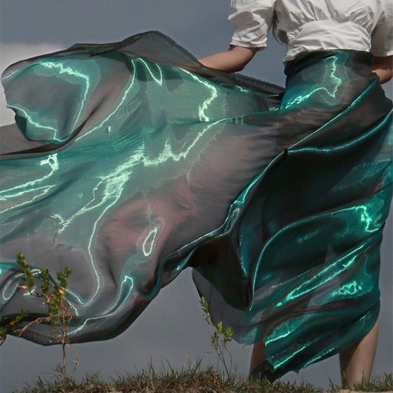 a woman in a white shirt and green skirt is walking on the grass with her hands behind her back