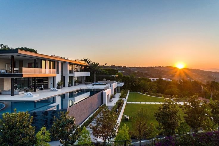 an aerial view of a modern house with the sun setting in the backround