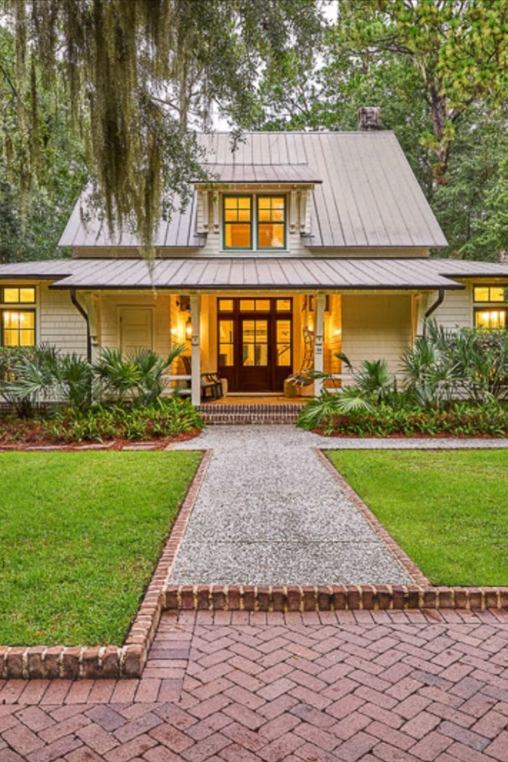 a white house with green grass and trees in the front yard, surrounded by brick pavers