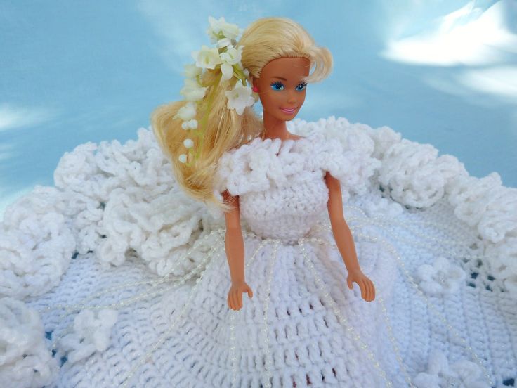 a doll with blonde hair wearing a white crochet dress and flower in her hair