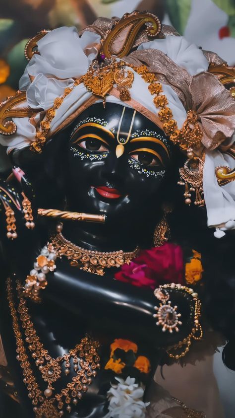 an idol is dressed in black and gold with flowers on it's head, holding a pipe