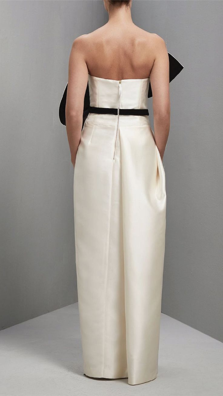 the back of a woman wearing a white dress with black trims and an asymmetrical belt