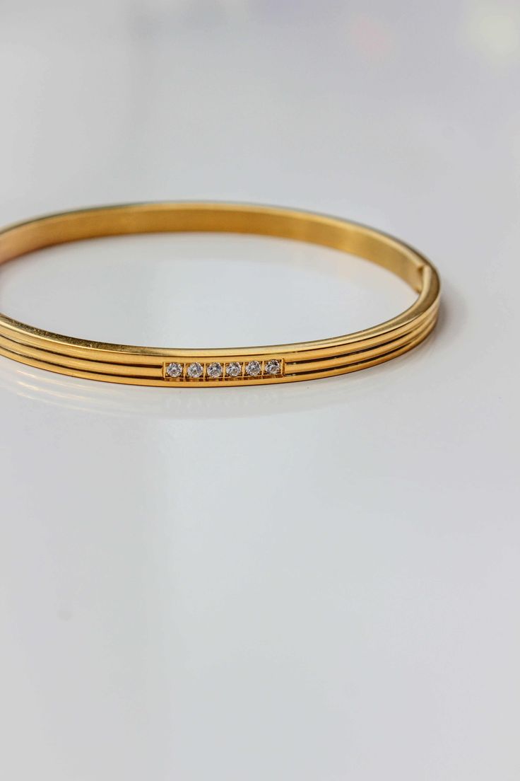 PRODUCT DESCRIPTION The bangle celebrates the beauty of expert craftsmanship. Formed from polished titanium steel and coated with gleaming18-karat gold for an opulent finish, this bangle adds a suave touch to your wrist – whether worn alone or stacked alongside your favorite timepiece. Signature Gold Bangle Water Resistant 18k Gold-plated on titanium steel Zirconia One Size: Oval Shape that fits small wrists from 14-16cm Read our full Jewellery Care Guide here Read our Sizing Guide here Classic Stainless Steel Bangle For Formal Occasions, Timeless Stainless Steel Bangle Bracelet, Adjustable Gold Bangle For Everyday Luxury, Yellow Gold Stainless Steel Bangle, Formal Stainless Steel Bangle With Polished Finish, Gold Stainless Steel Bangle, Tarnish Resistant, Minimalist Stainless Steel Bangle For Formal Occasions, Luxury Stainless Steel Bangle Bracelet, Tarnish Resistant Stainless Steel Gold Bangle