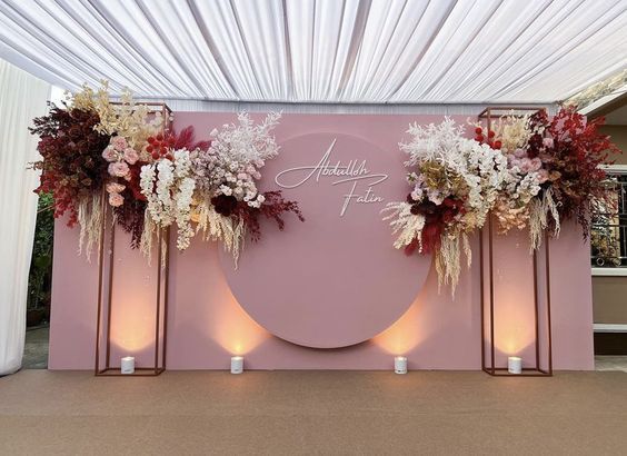 a pink backdrop with flowers and candles on the side for a wedding ceremony at an outdoor venue