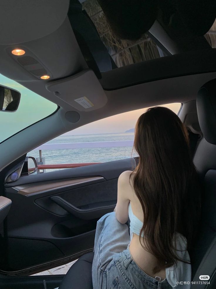 a woman sitting in the back seat of a car looking out at the ocean and mountains