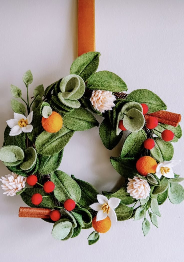 a green wreath with oranges, white flowers and leaves hanging on a wall next to a wooden frame