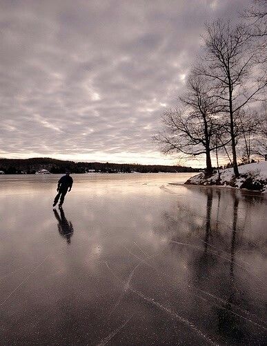 a man skating on an ice covered lake at dusk with trees in the background and clouds in the sky