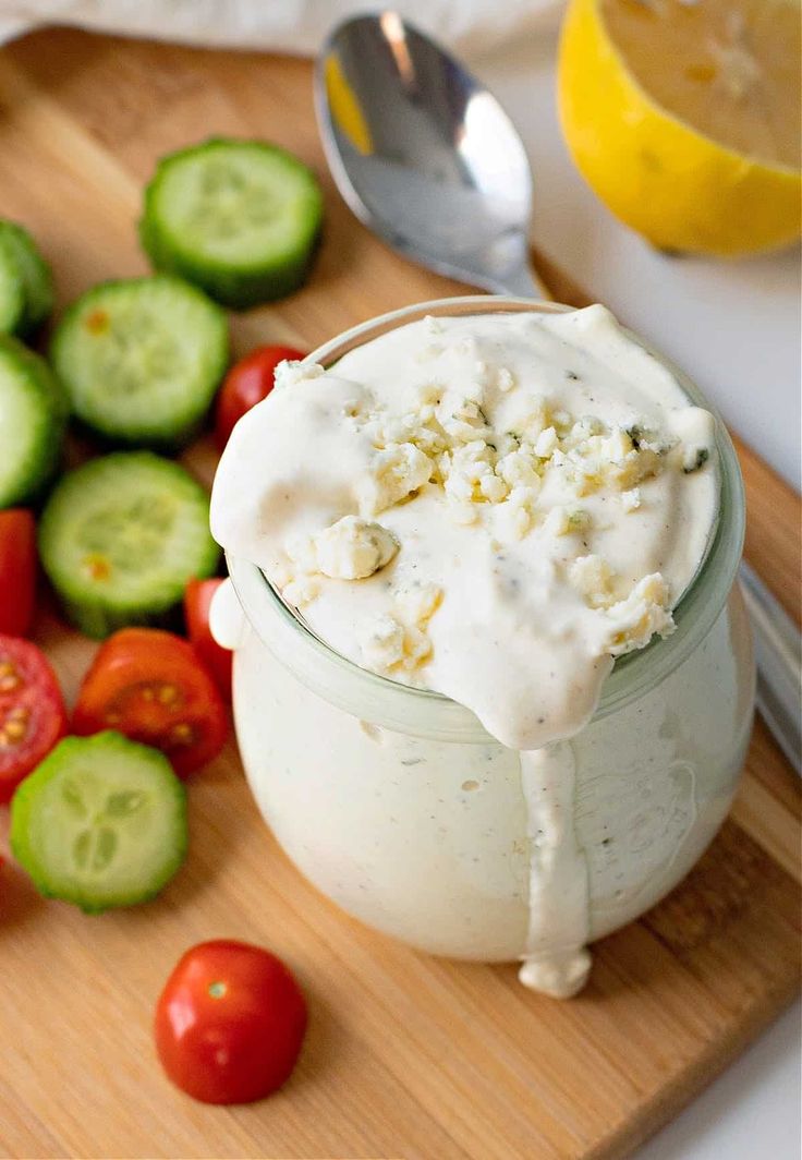 a wooden cutting board topped with cucumbers, tomatoes and other vegetables next to a jar of mayonnaise