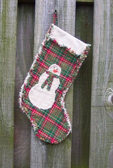 a christmas stocking hanging on a fence with a snowman in the center and plaid fabric