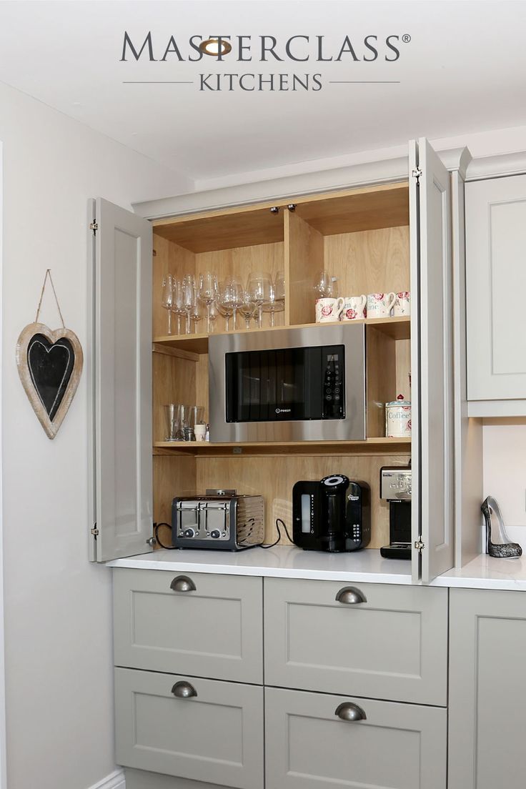 a kitchen with white cabinets and gray countertops has a microwave, toaster, coffee maker and wine glasses on it