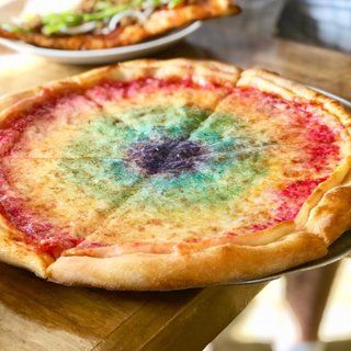 two pizzas with different colored toppings sitting on top of a wooden table next to each other