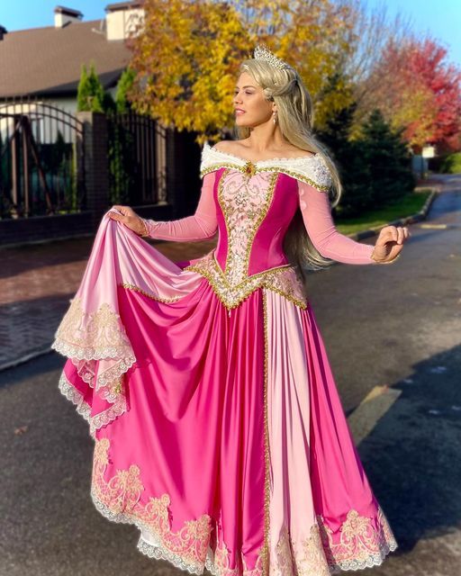 a woman in a pink and gold dress is standing on the street with her arms outstretched