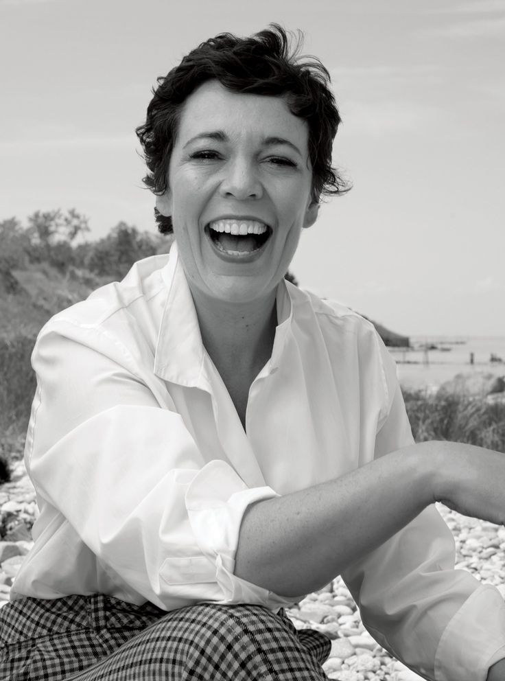 black and white photograph of woman sitting on rocks with mouth open, smiling at camera