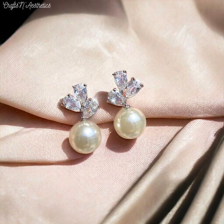 Zirconia Leaf Stud Earring | Pearl Bridal Earring | Wedding Jewelry for Her | Bridesmaids Gifts | Pearl Earring with Zirconia | Bridal Gift  🛍️Welcoming our newest addition of earrings! A gorgeous harmony of A Pearl Ball Pendant and leaf patterned Cubic Zirconia Crystals!  🌼 Whats included: 1 x Pair of Cubic Zirconia Leaf Patterned Crystal with Pearl Pendant Earrings! (0.66 inches)   Choose between our 2 unique colors to fit your style, the way you like! White | Gold  Fast Handmade Process 14-Day Return and Exchange Period HandCrafted & Handmade 🛍️ Here at CraftsNAesthetics our staff works hard to make sure each bracelet comes to you as perfect as possible! Our staff has 4 years of experience of making quality jewelry with durable and long-lasting materials to ensure you have gorgeous p Glamorous White Gold Crystal Earrings For Wedding, Glamorous White Gold Earrings For Wedding, Dazzling Diamond White Bridal Earrings For Wedding, Classic Diamond White Crystal Earrings For Weddings, Diamond White Cubic Zirconia Cluster Earrings For Wedding, White Gold Crystal Wedding Earrings, Diamond White Sparkling Stones Bridal Earrings For Wedding, Diamond White Sparkling Bridal Earrings For Wedding, Diamond White Bridal Earrings With Sparkling Stones For Wedding