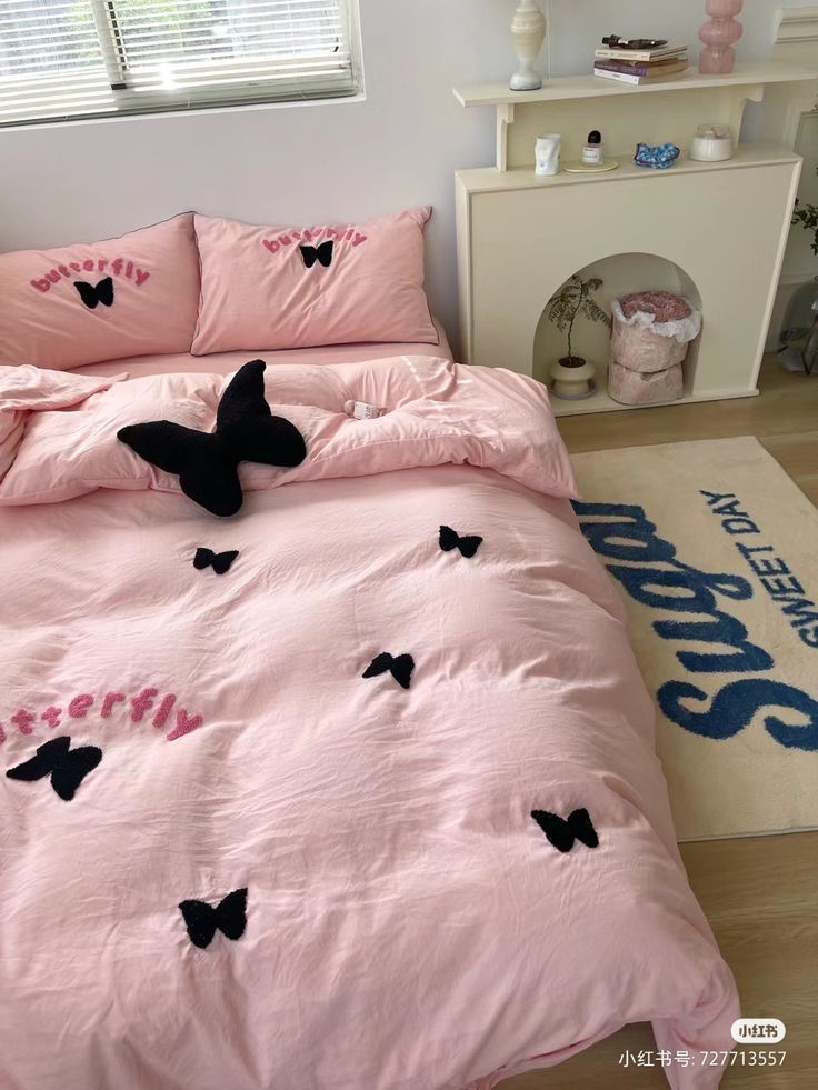 a pink bed with black butterflies on the comforter and pillow cases in front of a window