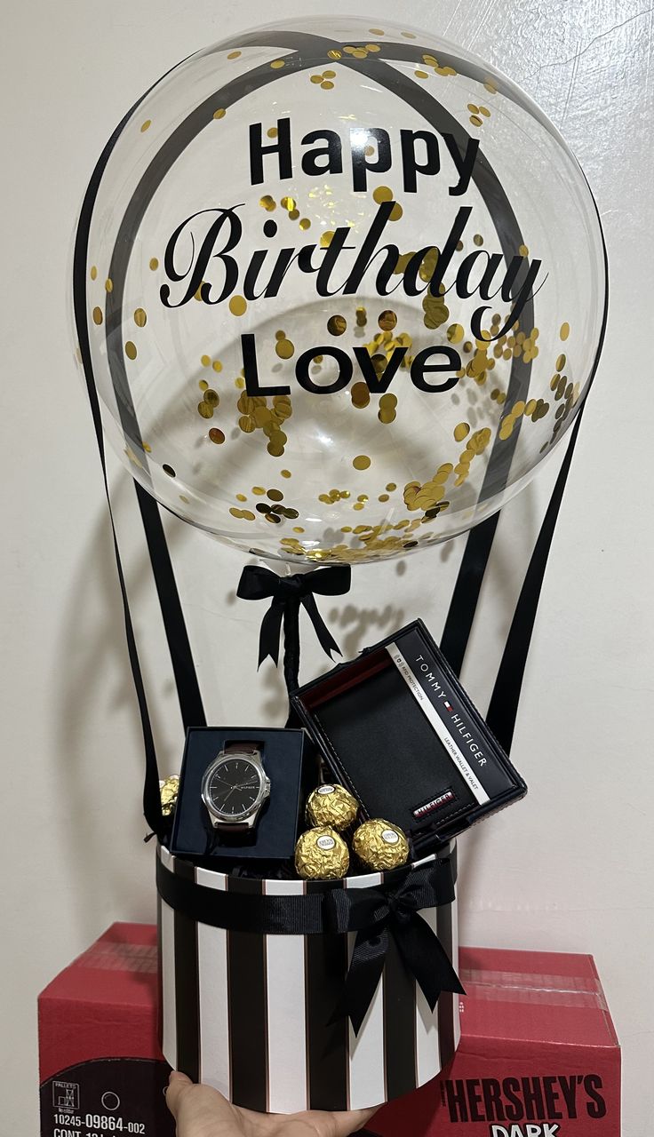 a birthday balloon with gold confetti and chocolates in it sitting on top of a box