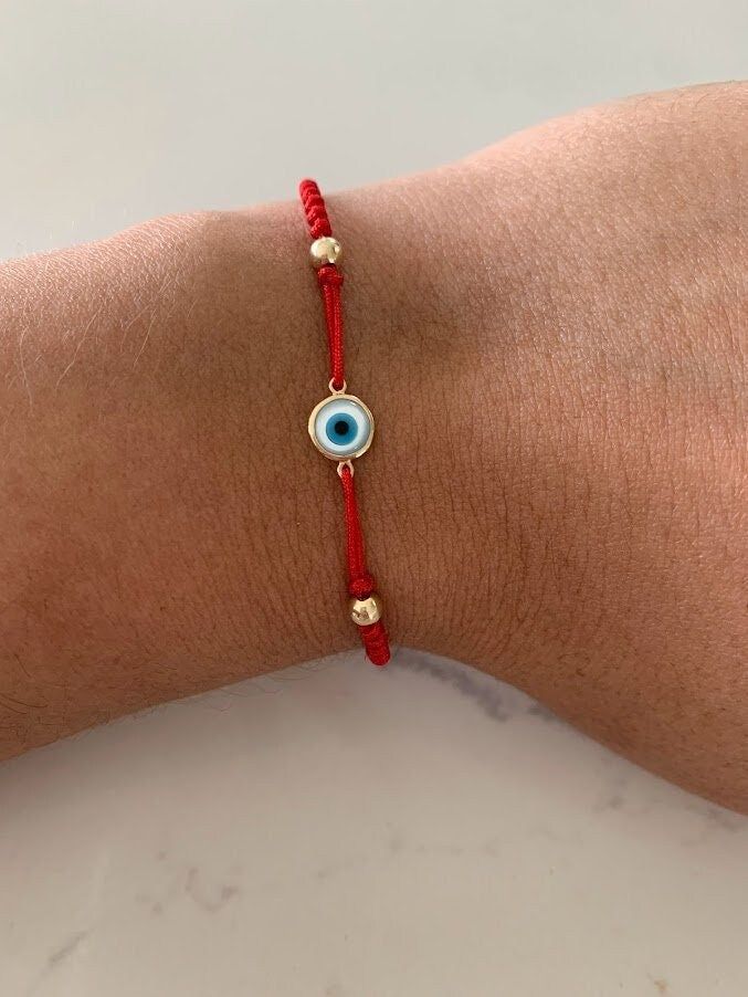 This 14K Solid Gold Evil Eye Bracelet is adorned by a luxurious 7MM Mother of Pearl design. Stretchable and handmade, it makes a perfect gift for any occasion. It is Unisex ♦ Materials: Evil Eye is 14K Gold, Mother Pearl, 4 Beads Beads are Gold-filled   ♦ Available colors: Gold and Blue  ♦ Eye measurements: 7 MM PRODUCTION TIMES Order processing time varies between 1-4 business days, we work on our pieces daily All orders placed on Sunday, or on a national holiday will begin processing the follo Elegant Red Adjustable Braided Bracelets, Elegant Red Adjustable Braided Bracelet, Red Round Beads Bracelet As Gift, Elegant Red Beaded Friendship Bracelets, Red Jubilee Bracelet Jewelry Gift, Handmade Red Evil Eye Bracelet As A Gift, Handmade Red Evil Eye Bracelet For Gift, Red Bracelet Jewelry For Gifts, Handmade Red Evil Eye Bracelet Gift