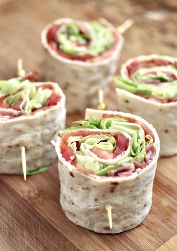 four wraps with meat and veggies are on a cutting board