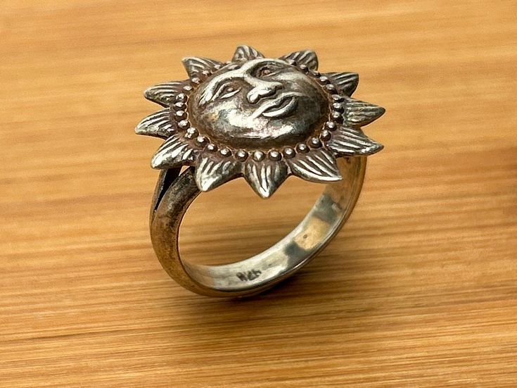 Capture the essence of vintage charm with this stunning sterling silver ring, featuring a radiant sun face design that vintage lovers will adore.  This unique piece exudes character and appeal, perfect for those who appreciate intricate sun motifs and the allure of a well-aged patina. The sun face, with its bulbous form and blank expression, showcases excellent attention to detail.  Encircled by a bead dot design, the face is further highlighted by beams of pointed light etched with lines to represent coronal streamers, adding depth and texture to the piece.  The ring's patina enhances its vintage appeal, giving it a timeless, well-loved look. Key Features: Material: Sterling Silver Marking: Band marked with 926 (slightly above the standard 925) Weight: 5.07 grams Size: Measures 6.75 Desig Vintage Silver Ring With Sun And Moon Design, Vintage Sun And Moon Design Rings As Gift, Vintage Sun And Moon Design Rings For Gift, Vintage Adjustable Rings With Sun And Moon Design, Adjustable Vintage Rings With Sun And Moon Design, Vintage Sun Design Jewelry Gift, Vintage Silver Jewelry With Sun Design, Vintage Sun And Moon Ring, Adjustable Vintage Jewelry With Sun Design