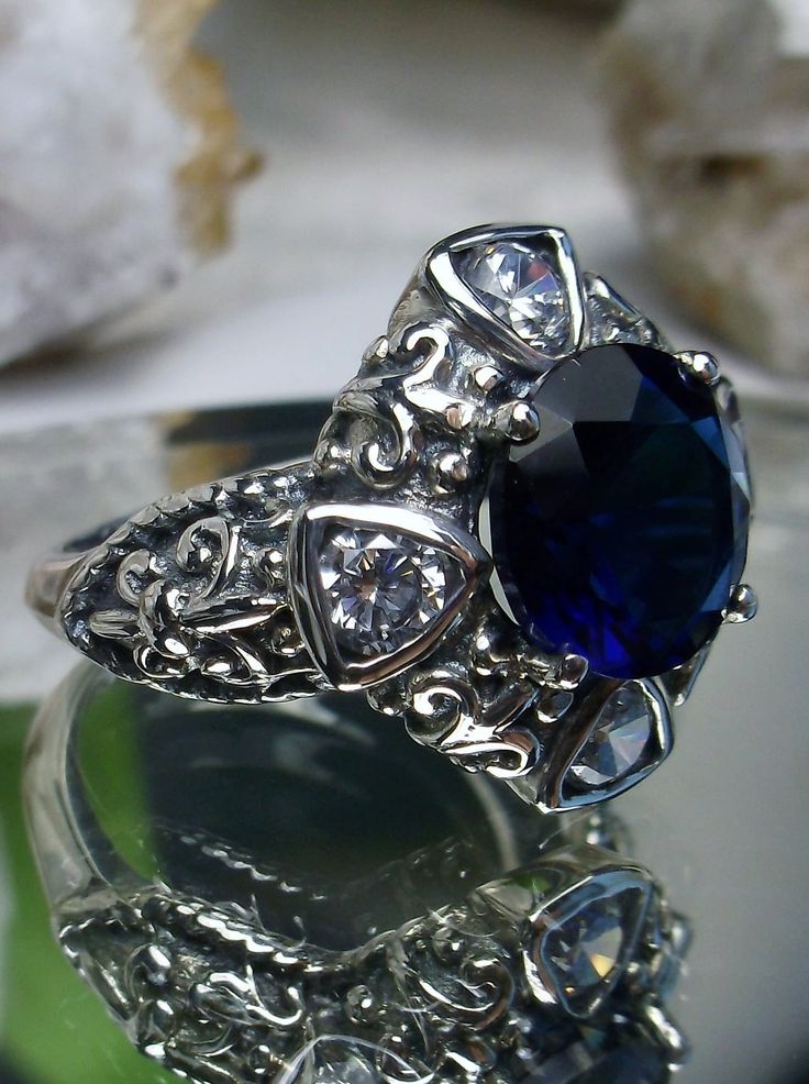 Blue Sapphire & White Cubic Zirconia (CZ) Sterling Silver RingRound5GemDeco Design#D138 Inspired by the stunning pieces of the early 1900s Art Deco movement, we have developed this gorgeous revival filigree ring in sterling silver. Meticulously handcrafted with a precision eye to detail, it's clear that no expense was spared in crafting this beauty. From its 925 silver markings to its beautiful Fleur de lis design surrounded by an array of dazzling white zirconia gems and one large high-quality Silver Crystal Rings With Stone Setting, Anniversary Crystal Rings With Stone Setting, Silver Sapphire Ring For Party, Elegant Silver Jeweled Ring, Silver Jeweled Party Rings, Silver Jeweled Crystal Wedding Ring, Silver Sapphire Ring With Stone Setting For Wedding, Wedding Sapphire Ring With Stone Setting In Silver, Jeweled Diamond Rings