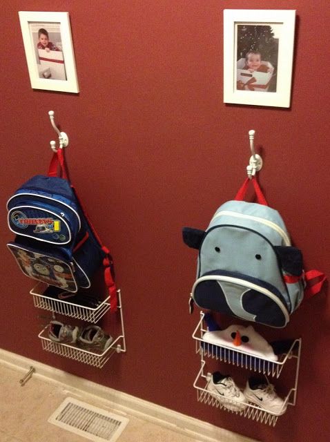 three backpacks hanging from hooks on a red wall with pictures and photos above them