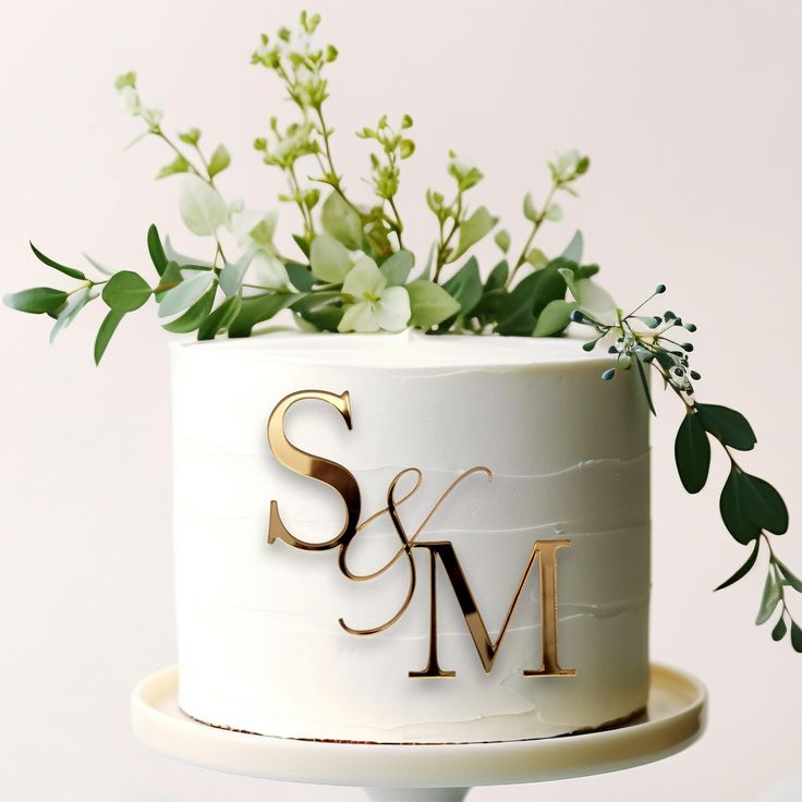 a wedding cake decorated with greenery and the letter s & m on it's side