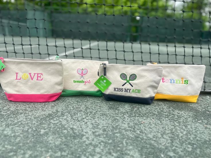 three tennis bags sitting on top of a tennis court next to a net with the words love tennis written on them