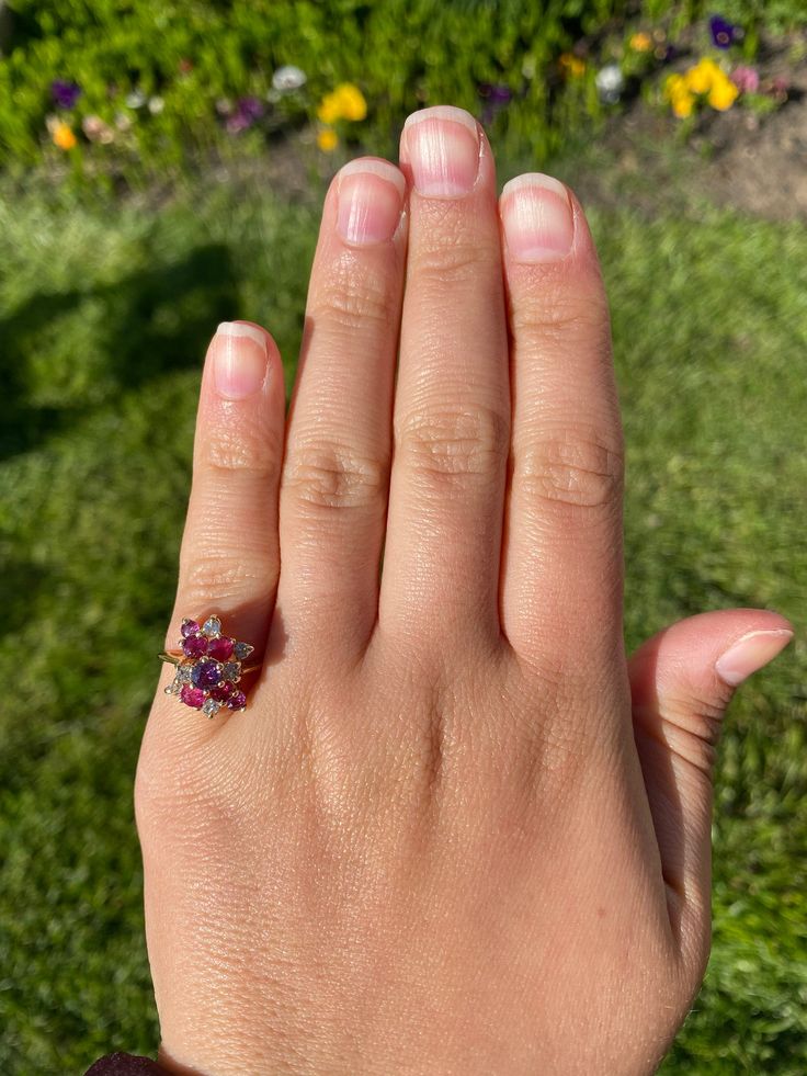 The Hempstead Bubblegum Ruby & Diamond Cocktail Ring. The ring features a reddish purple sapphire center stone with vivid red natural rubies and pink sapphires cascading from the center. Mixed between are diamonds throughout. The ring contains approximately 2 carats total weight by measurement of rubies and sapphires. The total estimated diamond weight by measurement is 0.36 carats. The ring is crafted in 14 karat yellow gold and is currently a finger size 6 yet can be adjusted to any finger Pink Diamond Cluster Ring With Multi-stone, Cluster Ruby Ring With Diamonds, Pink Ruby Diamond Ring With Multi-stones, Cluster Ruby Ring With Center Stone, Red Ruby Cluster Ring With Round Cut, Pink Ruby Rings With Multi-stone Detail, Pink Ruby Ring With Gemstone Accents, Pink Oval Multi-stone Ruby Ring, Red Multi-stone Sapphire Ring