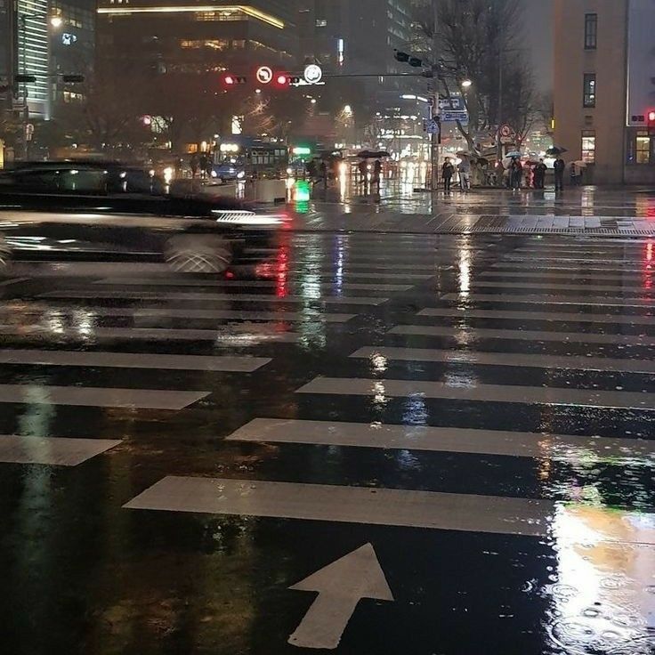 a city street at night with cars and people crossing the street in the rain,