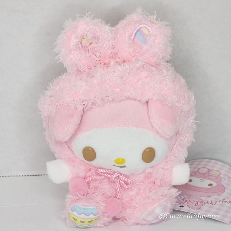 a pink teddy bear with fluffy fur on it's head and ears, sitting next to an egg