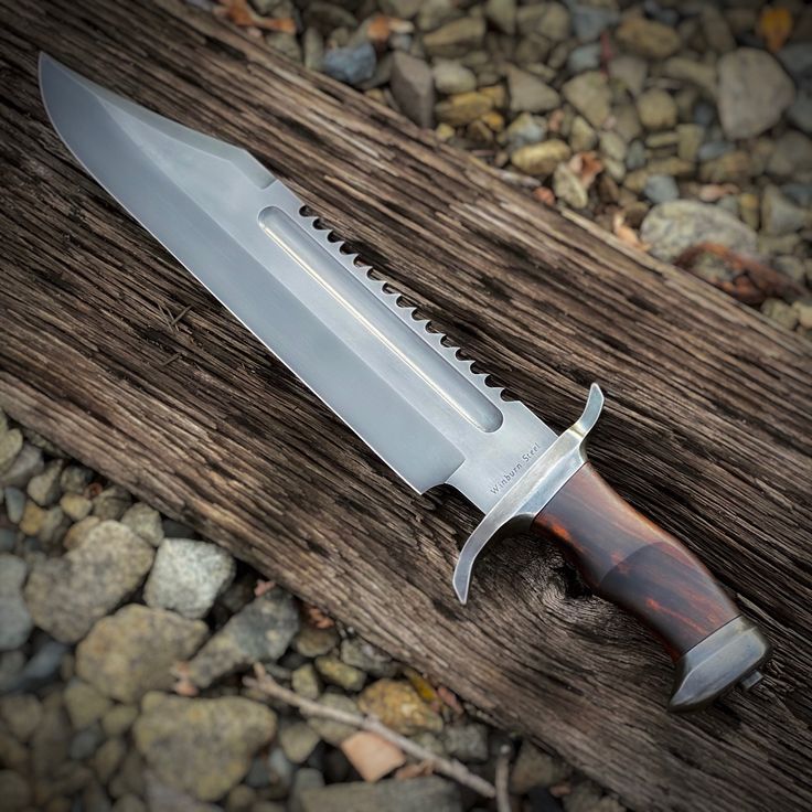 a large knife sitting on top of a wooden table next to rocks and gravel covered ground